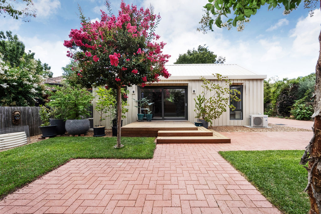 Modern backyard extension with cream cladding, timber deck and flowering crepe myrtle tree