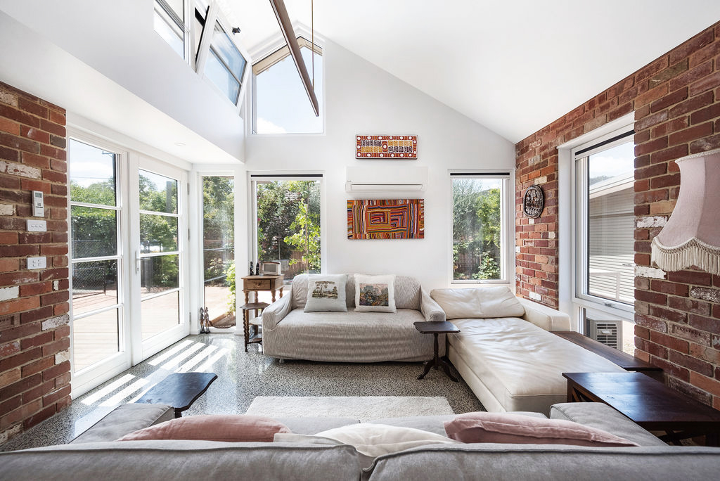 Light‑filled living room with exposed brick walls, large windows and vaulted ceiling