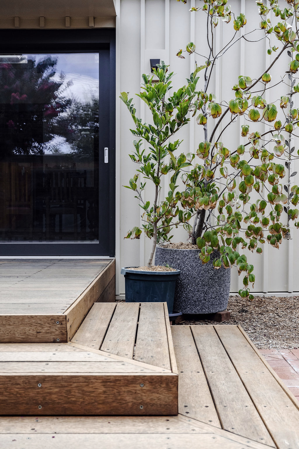 Close‑up of timber deck steps with potted plants beside sliding glass doors
