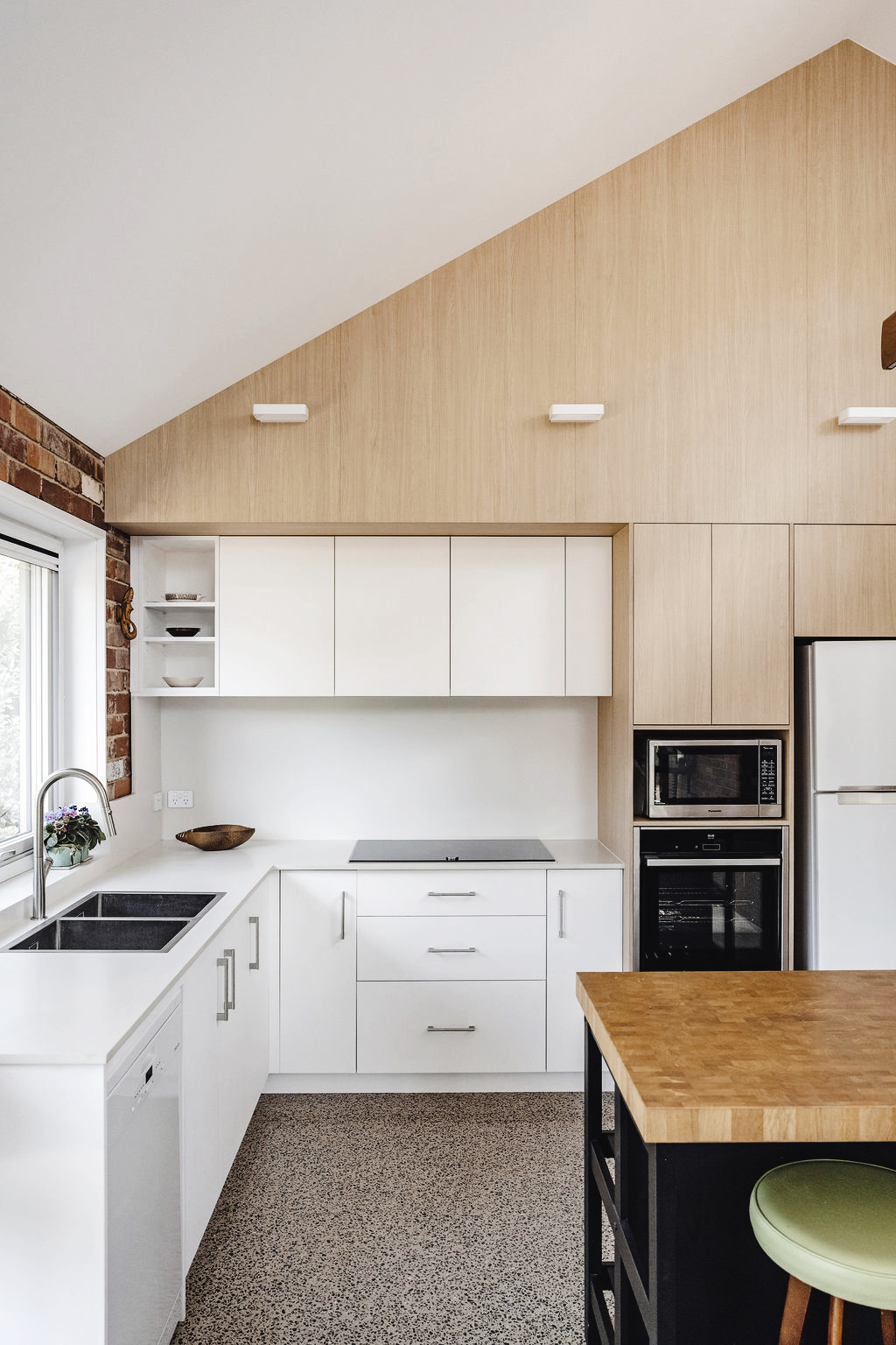 Contemporary kitchen with timber-lined pitched ceiling, white cabinetry and exposed brick accents