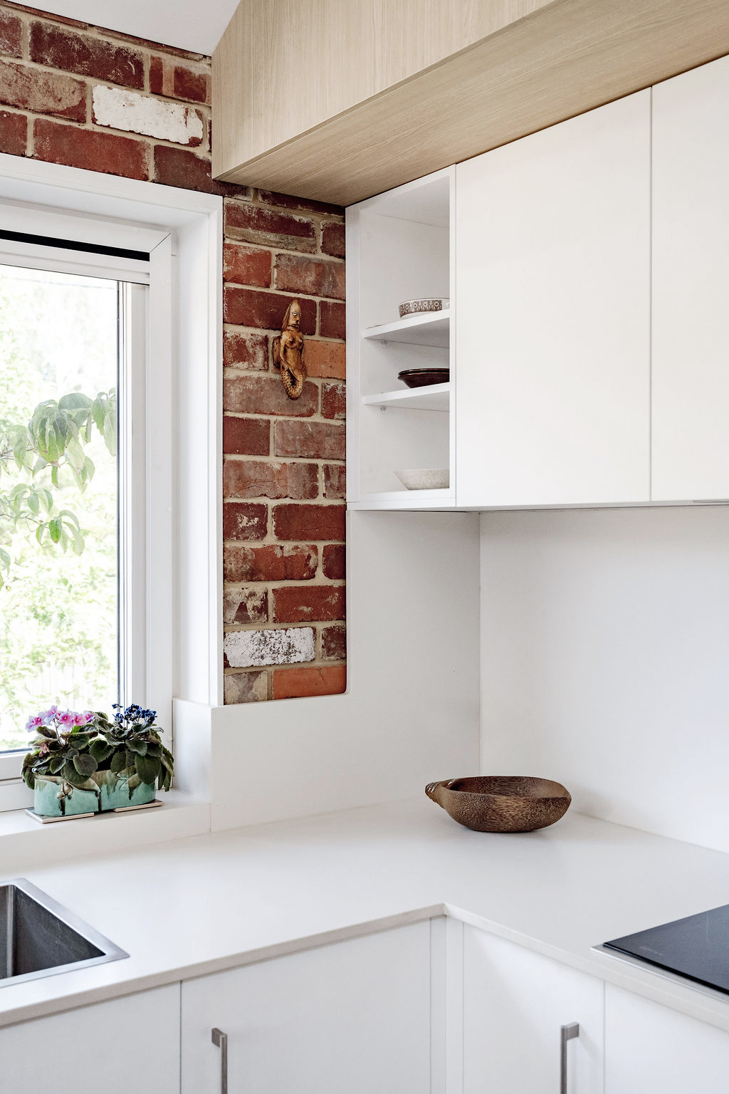 White kitchen with exposed brick feature wall, timber cabinetry and garden view