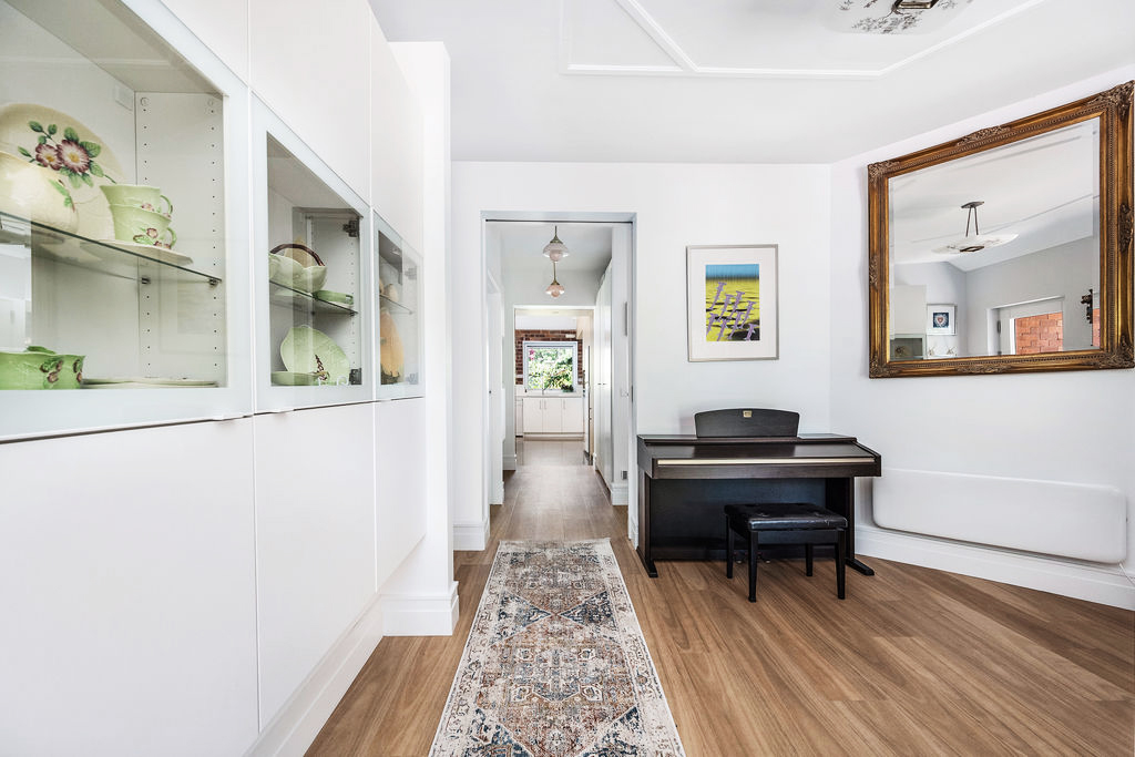 Bright hallway with timber floors, display cabinetry and piano leading to kitchen beyond