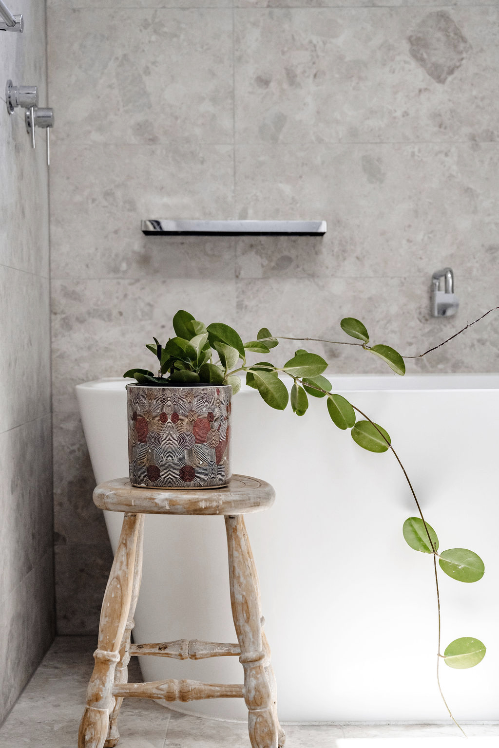 Freestanding bathtub with stone tile walls and potted plant on wooden stool