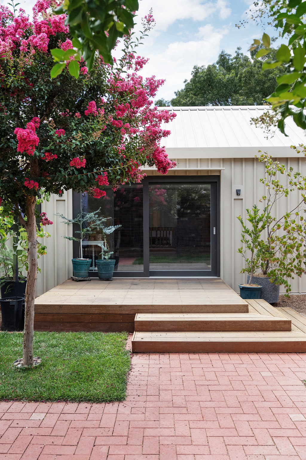 Modern rear deck with sliding glass doors, flowering crepe myrtle and potted plants