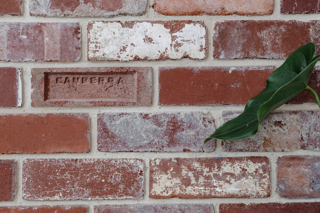 Red brick wall with weathered textures and a brick stamped ‘Canberra