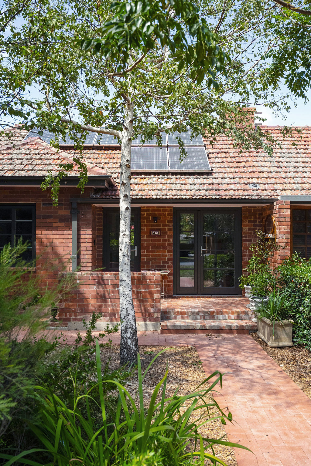 Renovated brick home with solar panels, black-framed doors and landscaped garden path